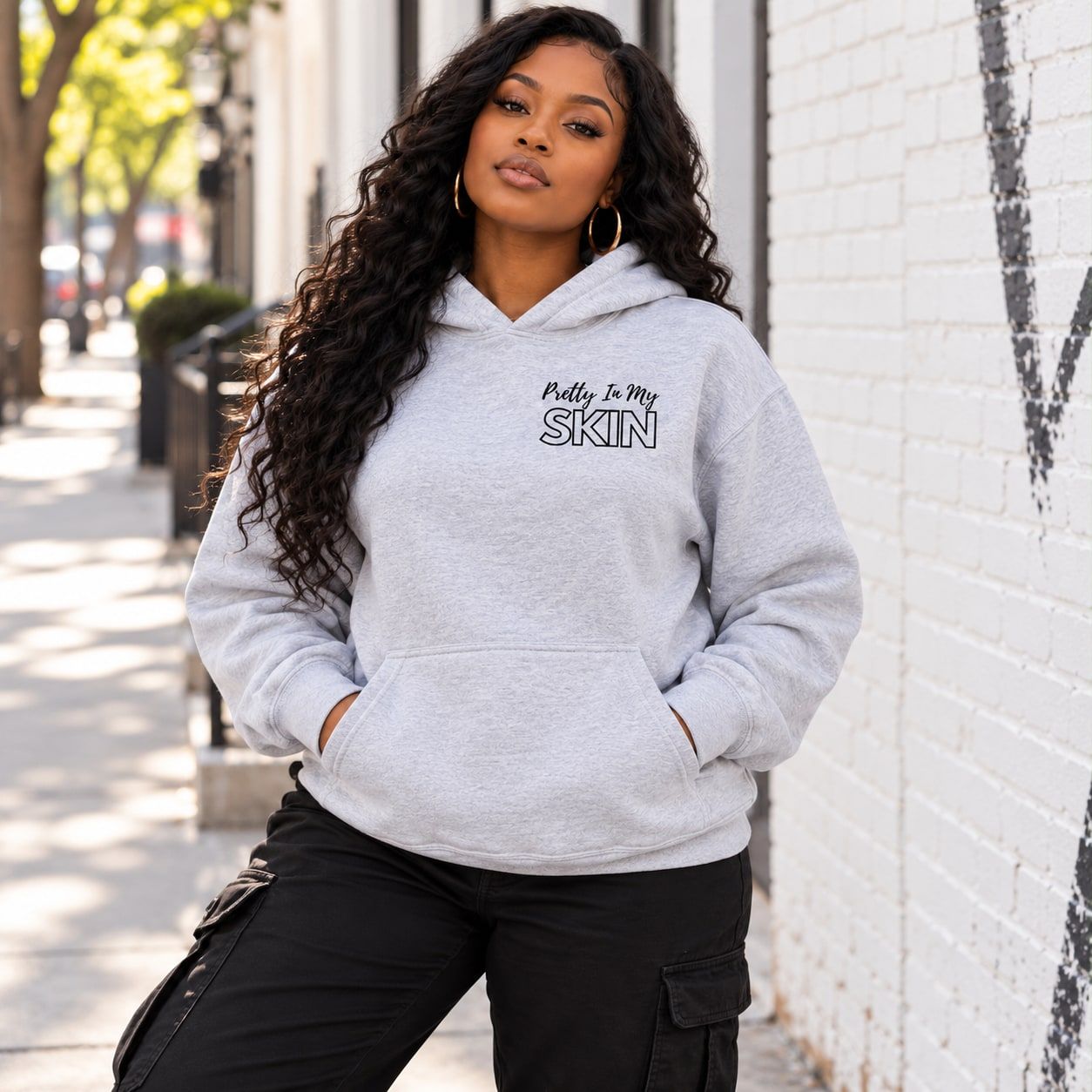 Woman in the ash grey hoodie showing the Pretty In My Skin chest print