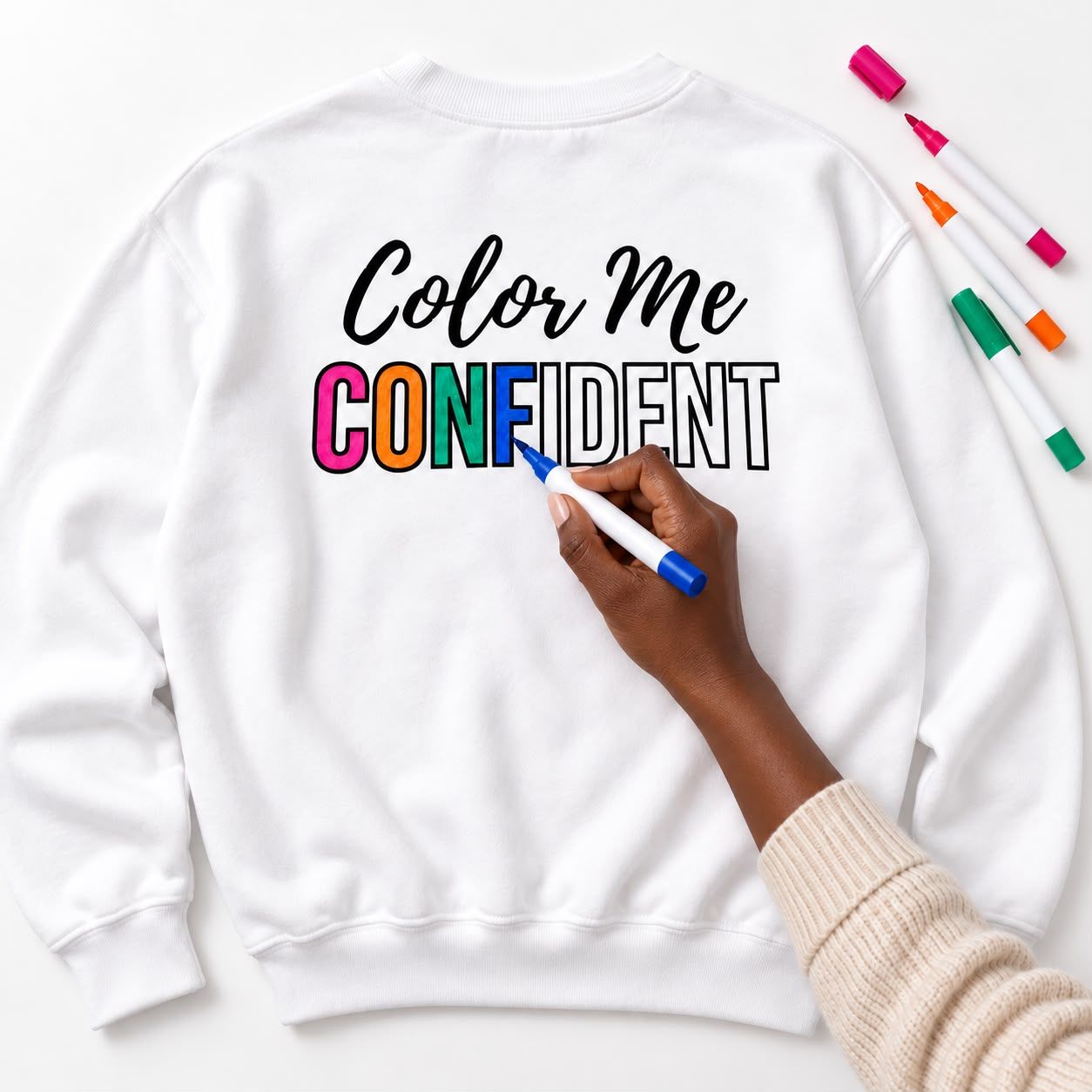 Hand coloring the CONFIDENT letters on a white crewneck