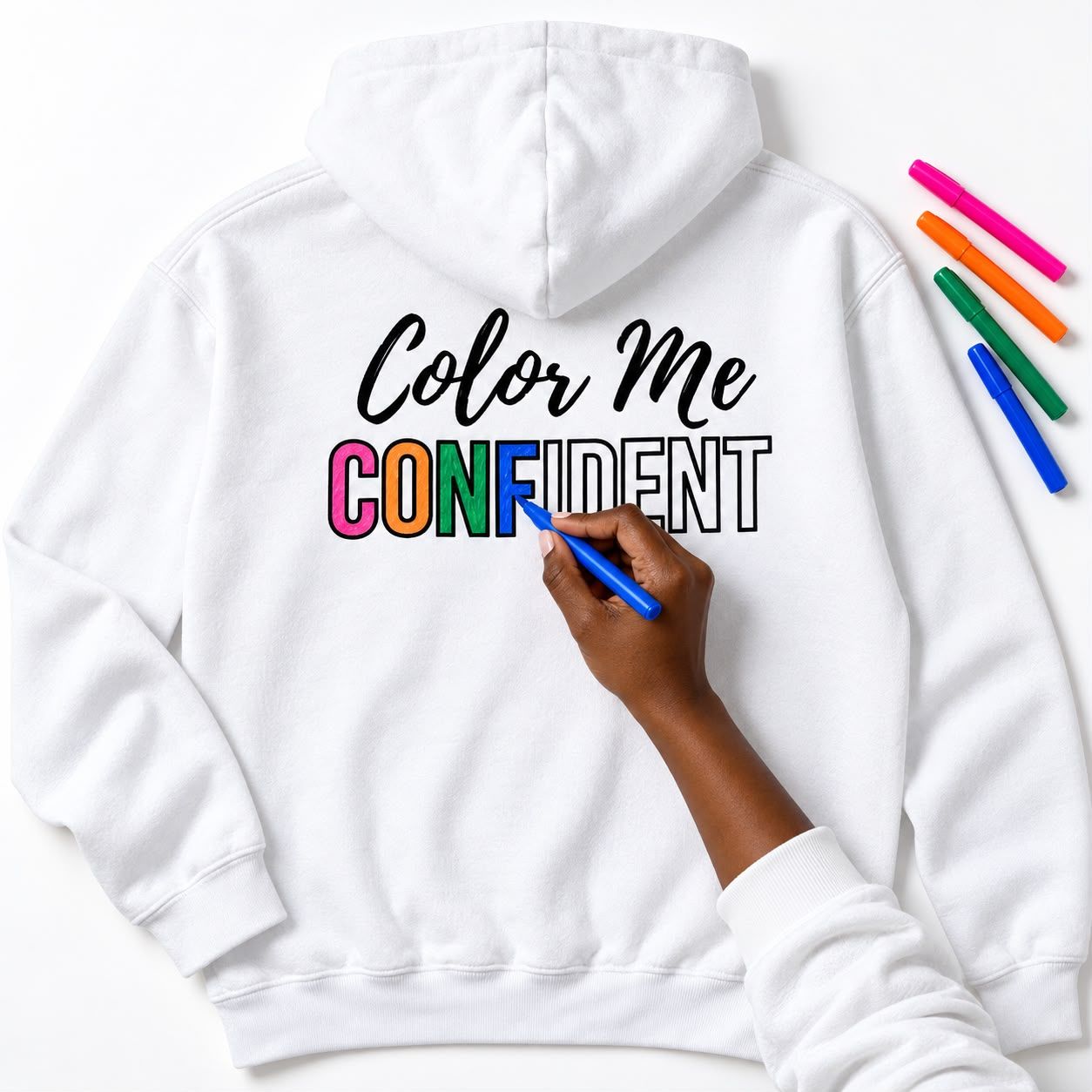 Hand coloring the CONFIDENT letters on a white hoodie with fabric markers